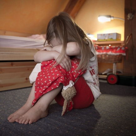 Ein kleines Mädchen sitzt weinend auf dem Fußboden in ihrem Zimmer. F