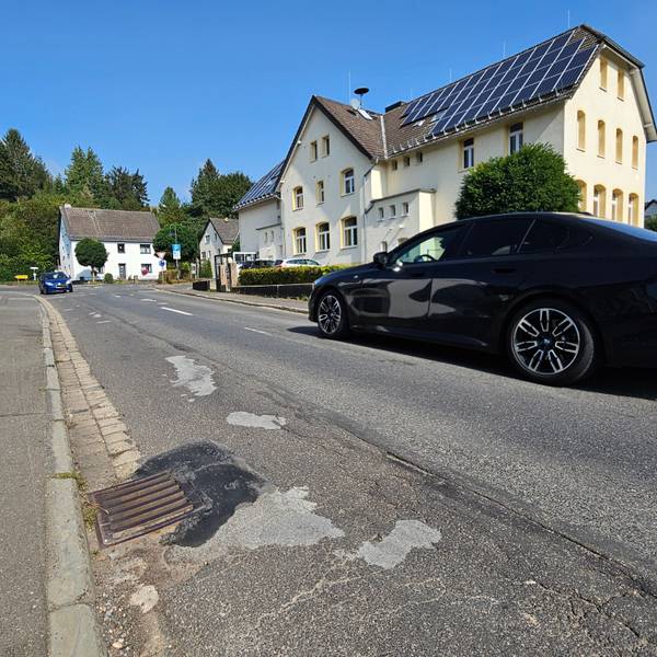 Zu sehen ist die Straße mit vielen geflickten Stellen. Zwei Autos kommen sich entgegen.