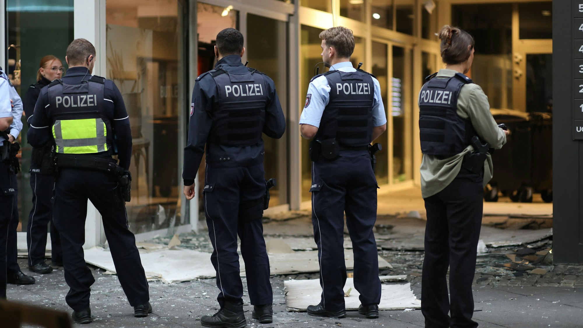 Polizisten stehen vor einem zerstörten Hauseingang.