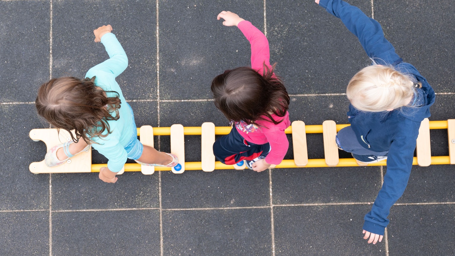 Kinder balancieren während eines Pressetermins auf dem Spielplatz einer Kindertagesstätte auf einem Brett.