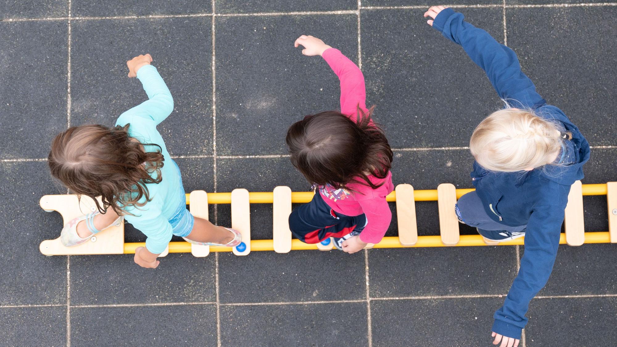 Kinder balancieren während eines Pressetermins auf dem Spielplatz einer Kindertagesstätte auf einem Brett. (zu dpa: «Viele Eltern müssen mit höheren Beiträgen für die Kita rechnen») +++ dpa-Bildfunk +++