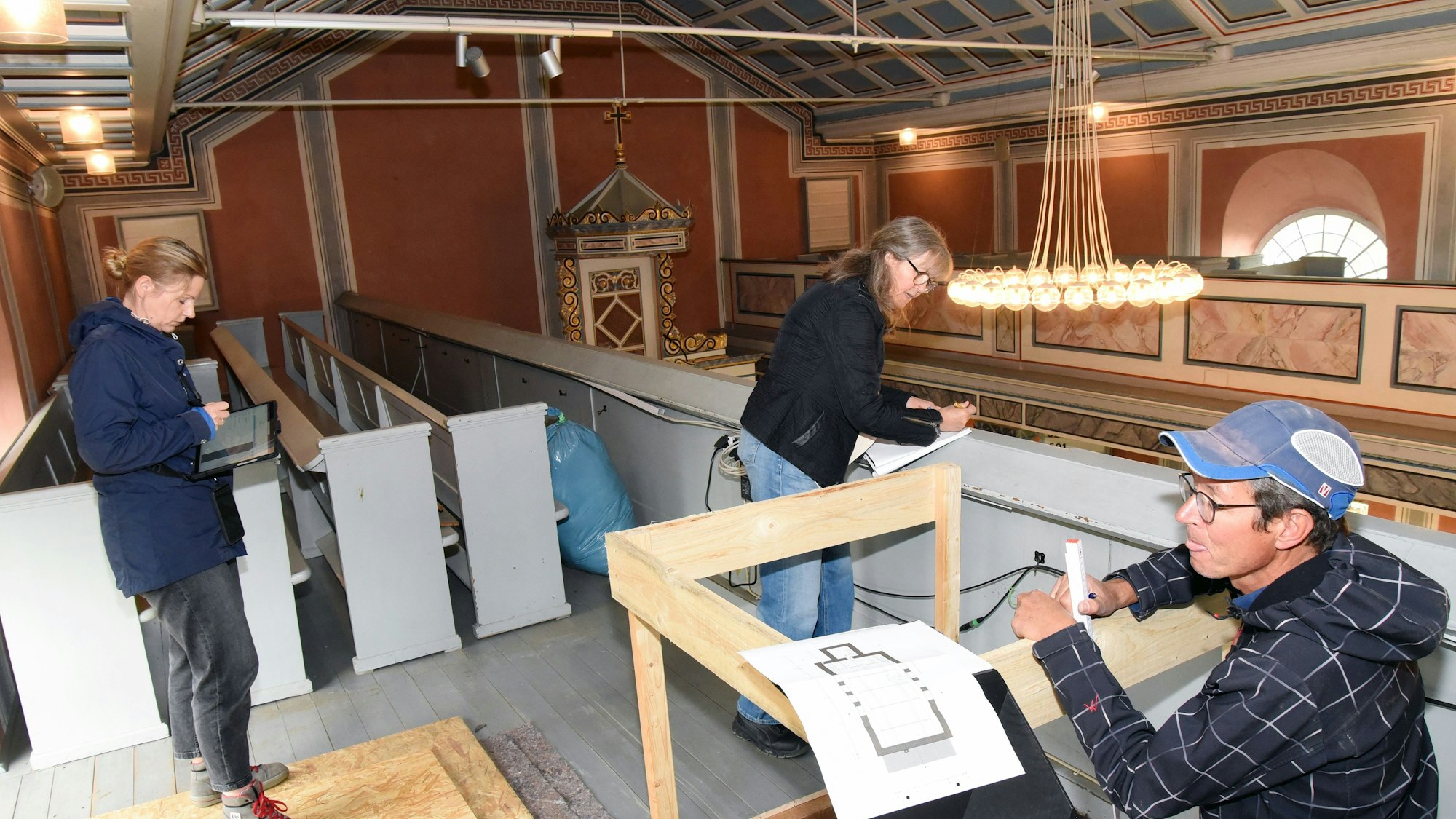 Das Foto zeigt zwei Frauen und einen Mann, die im Inneren einer Kirche das Gebäude untersuchen.