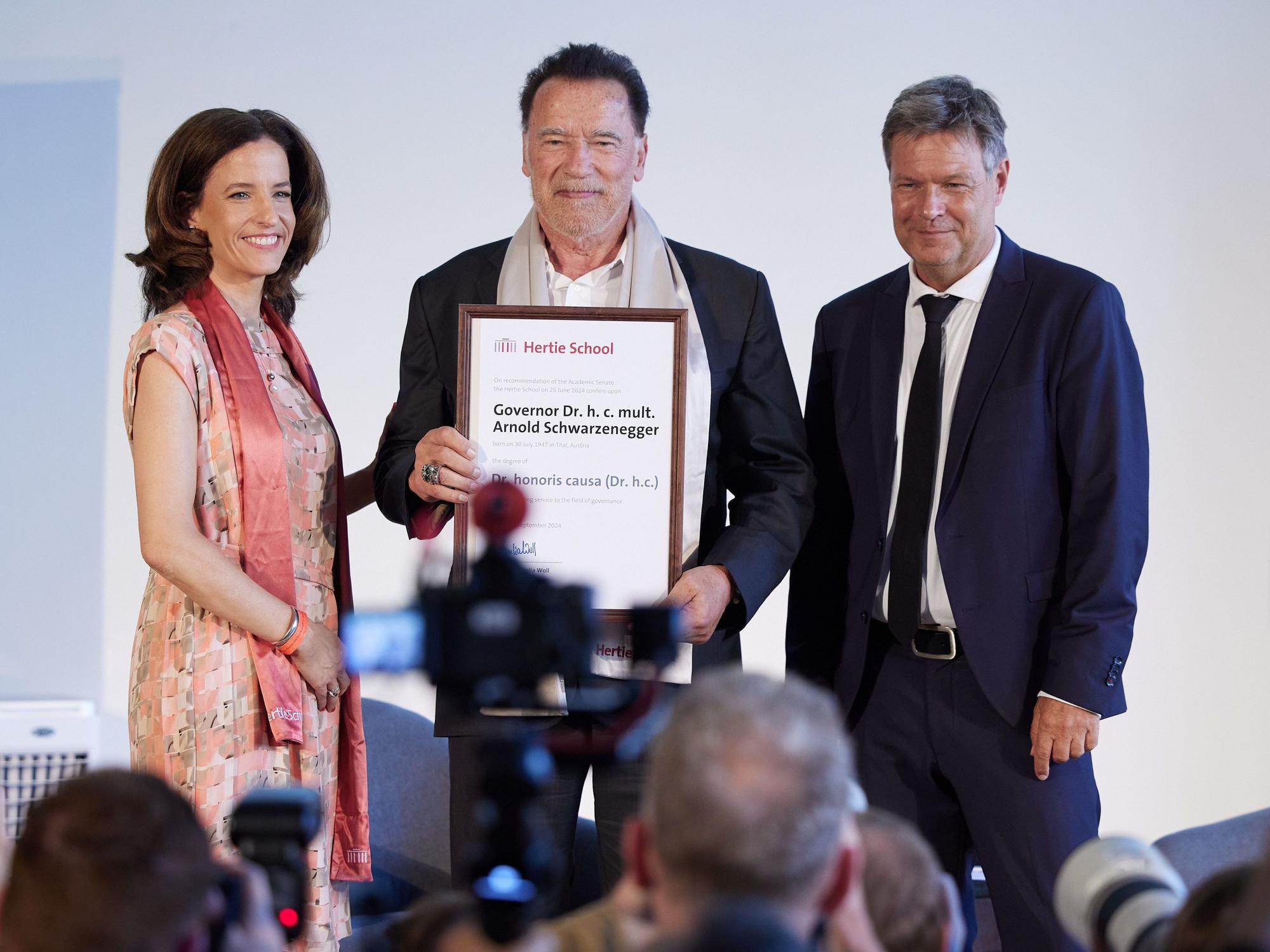 Arnold Schwarzenegger bekommt von Cornelia Woll und Robert Habeck die Ehrendoktorwürde zu verleihen. Schwarzenegger bekommt die Auszeichnung als „engagierter Kämpfer für Klimaschutz und zivilgesellschaftliches Engagement“.