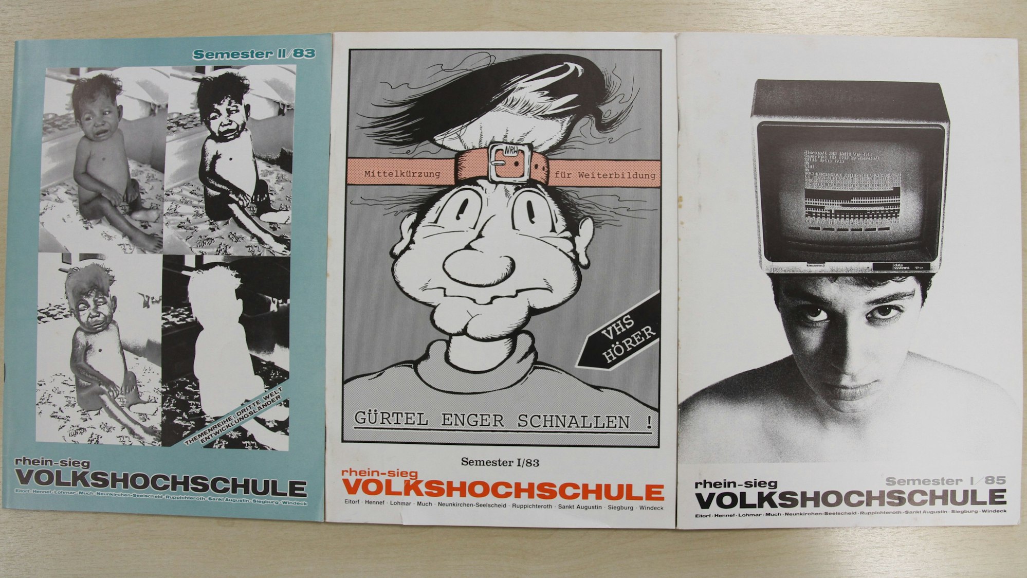 Drei VHS-Programmhefte auf einem Holztisch