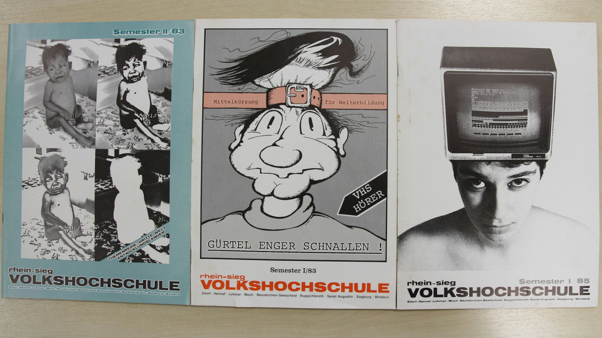 Drei VHS-Programmhefte auf einem Holztisch