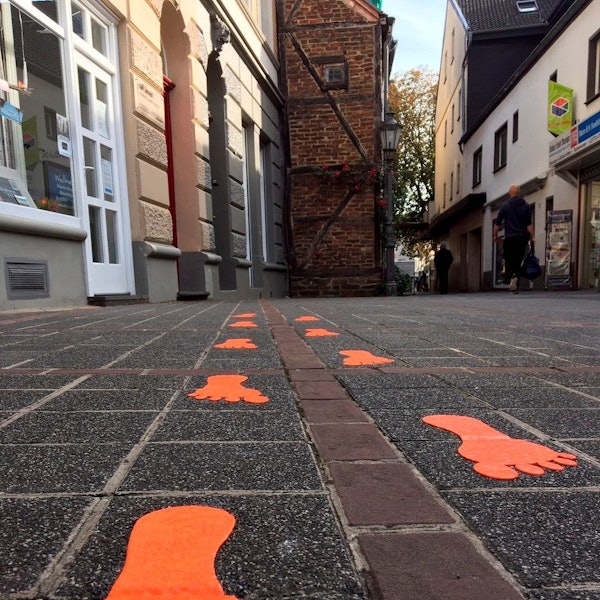Das Bild zeigt im Rahmen des Projekts "Bespielbare Stadt" farbige Fußspuren auf dem Pflaster der Kirchstraße in Brühl.