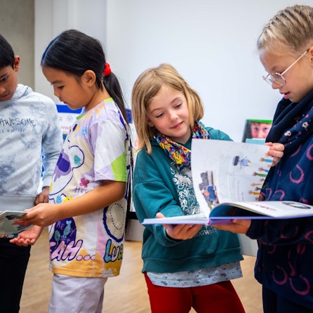 Das Bild zeigt drei Mädchen und einen Jungen, die in zwei Büchern blättern.
