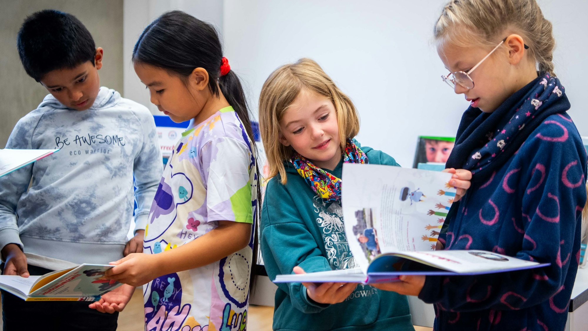 Das Bild zeigt drei Mädchen und einen Jungen, die in zwei Büchern blättern.