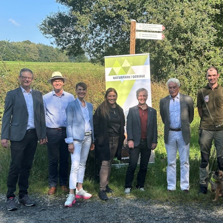 Fünf Männer und eine Frau vor einem Werbeschild