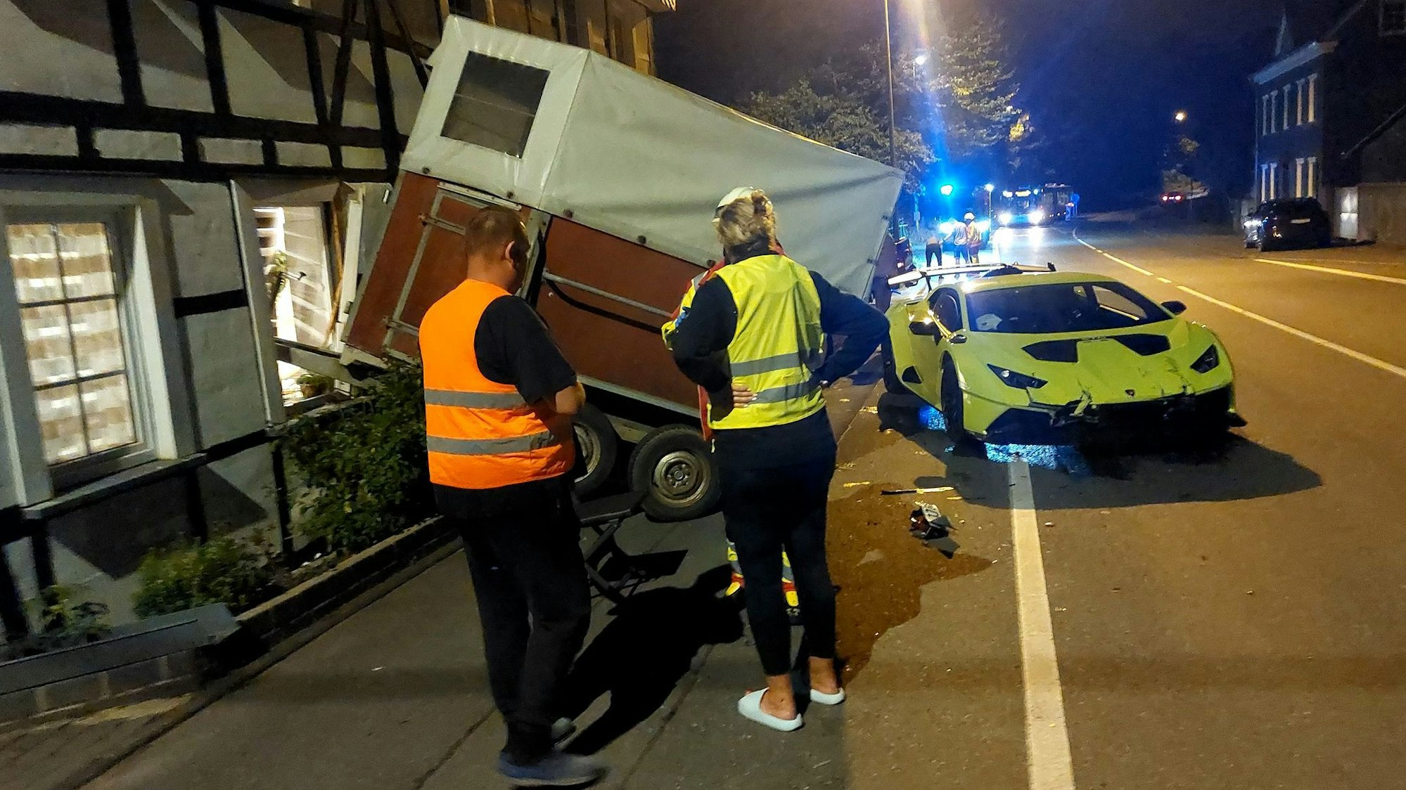 Zwei Menschen stehen in der Dunkelheit vor einem Unfallauto.