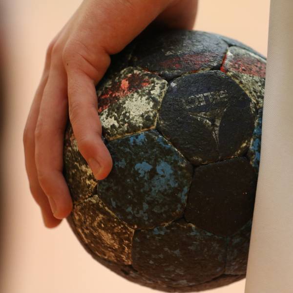 Ein beinahe schwarzer Handball liegt in einer Hand.