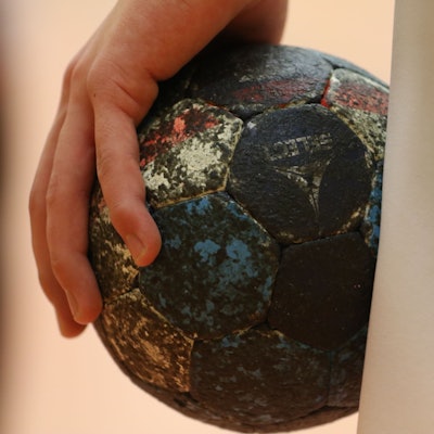 Ein beinahe schwarzer Handball liegt in einer Hand.