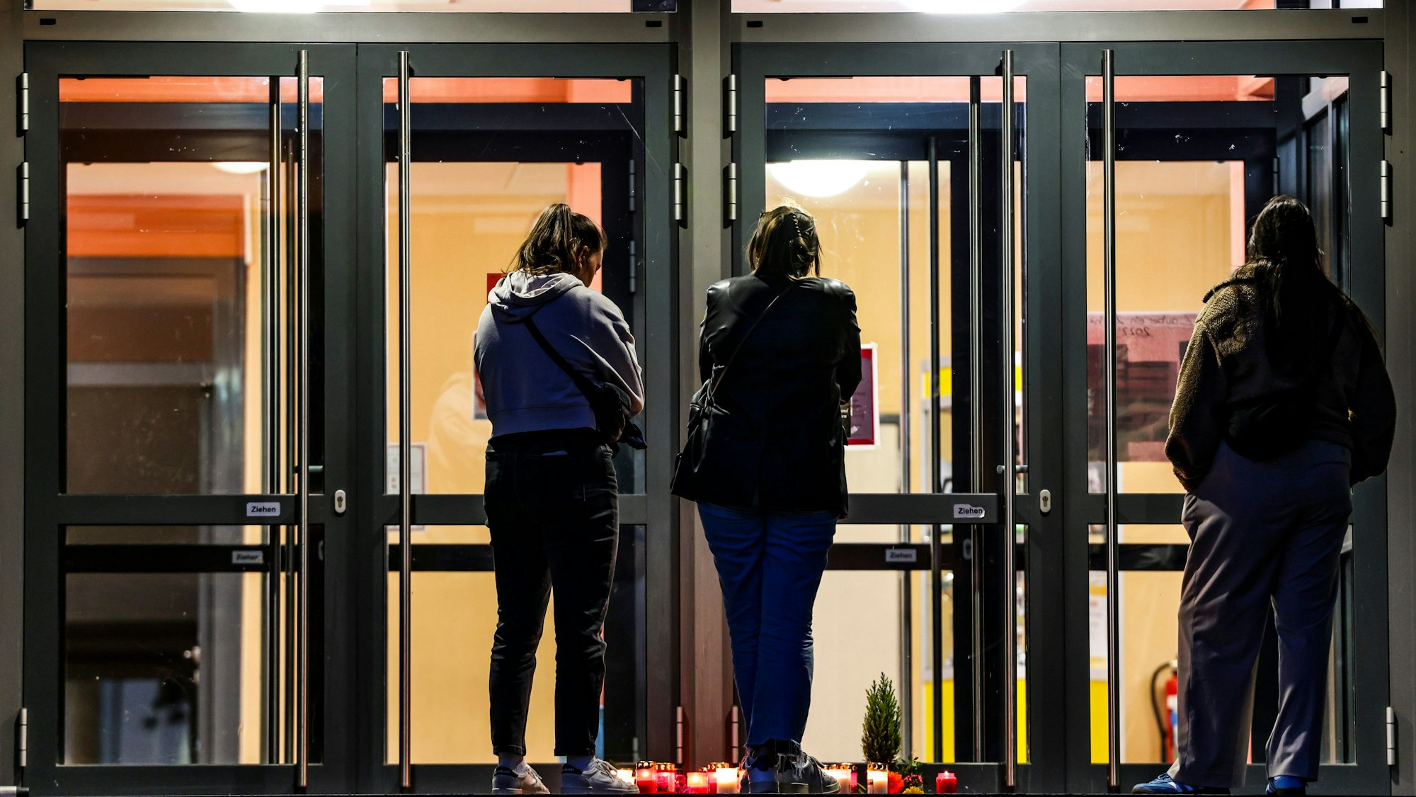 Drei Frauen trauern vor dem Eingang der Gesamtschule Duisburg-Mitte, auf dem Boden stehen Kerzen.