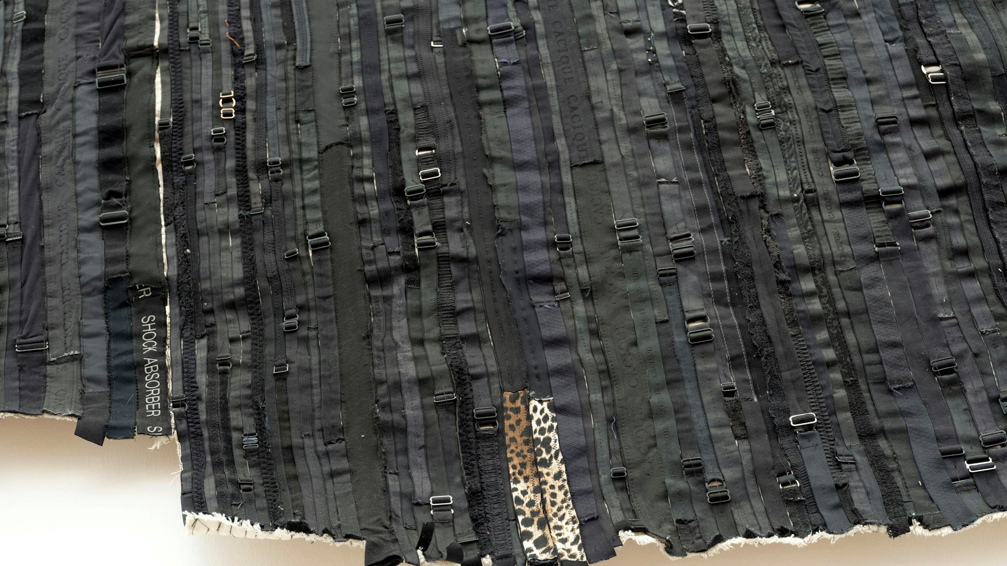 Schwarze BH-Bänder sind zu einer Collage vernäht.