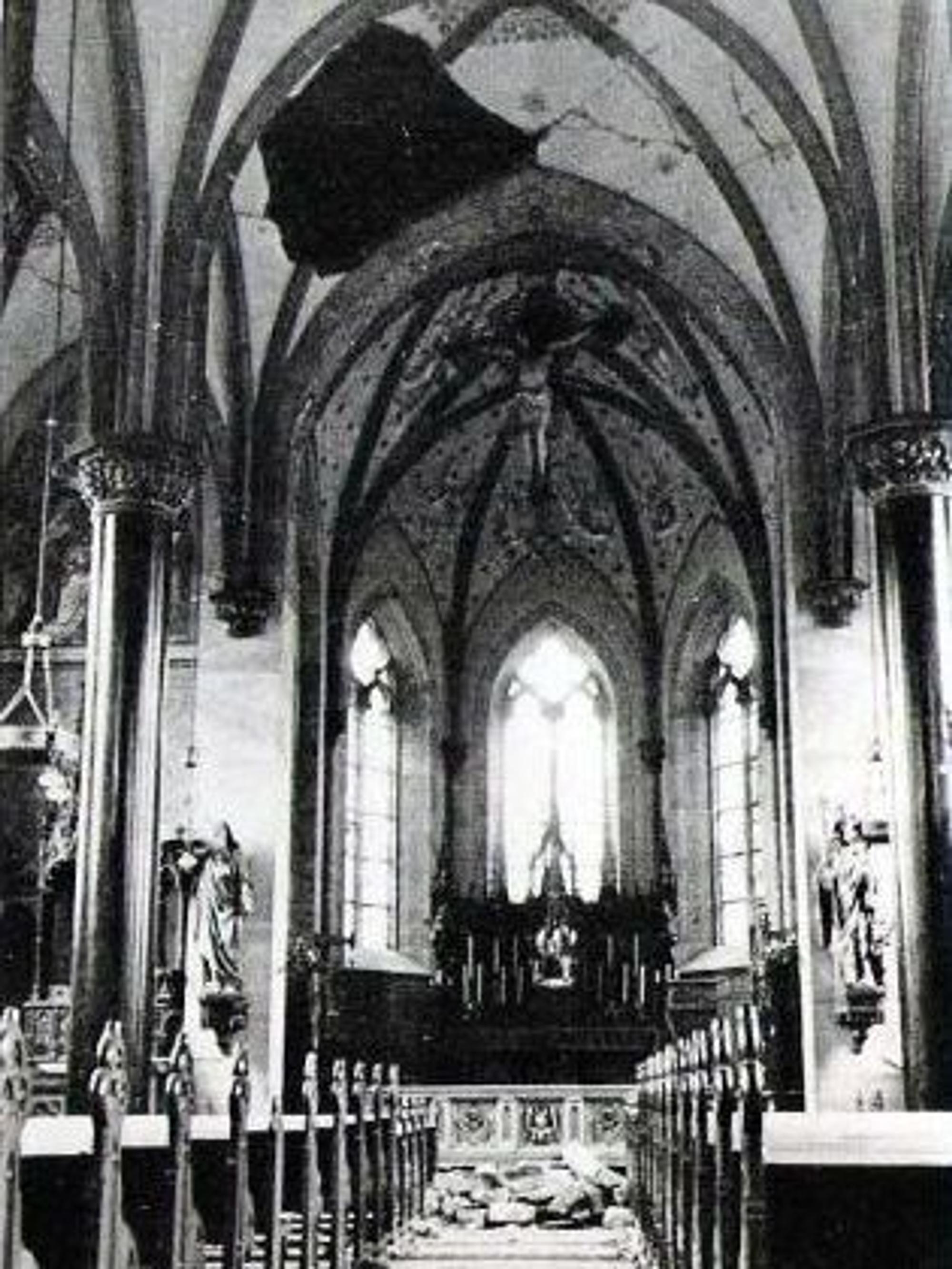 Ein schwarz-weiß Bild des Innenraums einer Kirche. Im Gewölbe ist ein großer Teil herausgebrochen und eingestürzt.