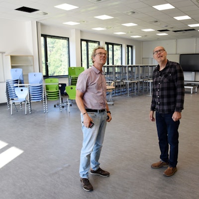 Zwei Männer stehen in einem modernen Klassenraum, sie schauen auf die Deckenverkleidung.