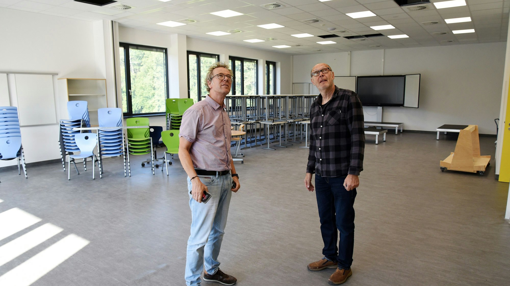 Zwei Männer stehen in einem modernen Klassenraum, sie schauen auf die Deckenverkleidung.