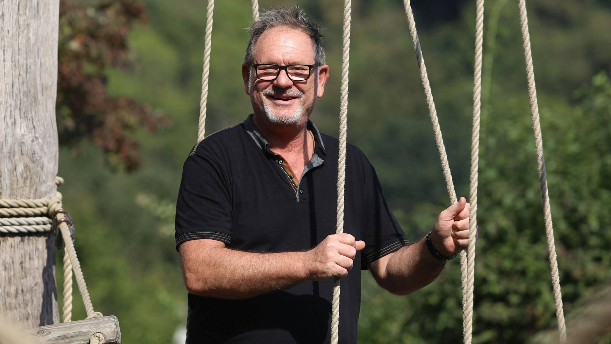 Ein Mann in schwarzem Poloshirt auf einer Kletterburg mit Seilen