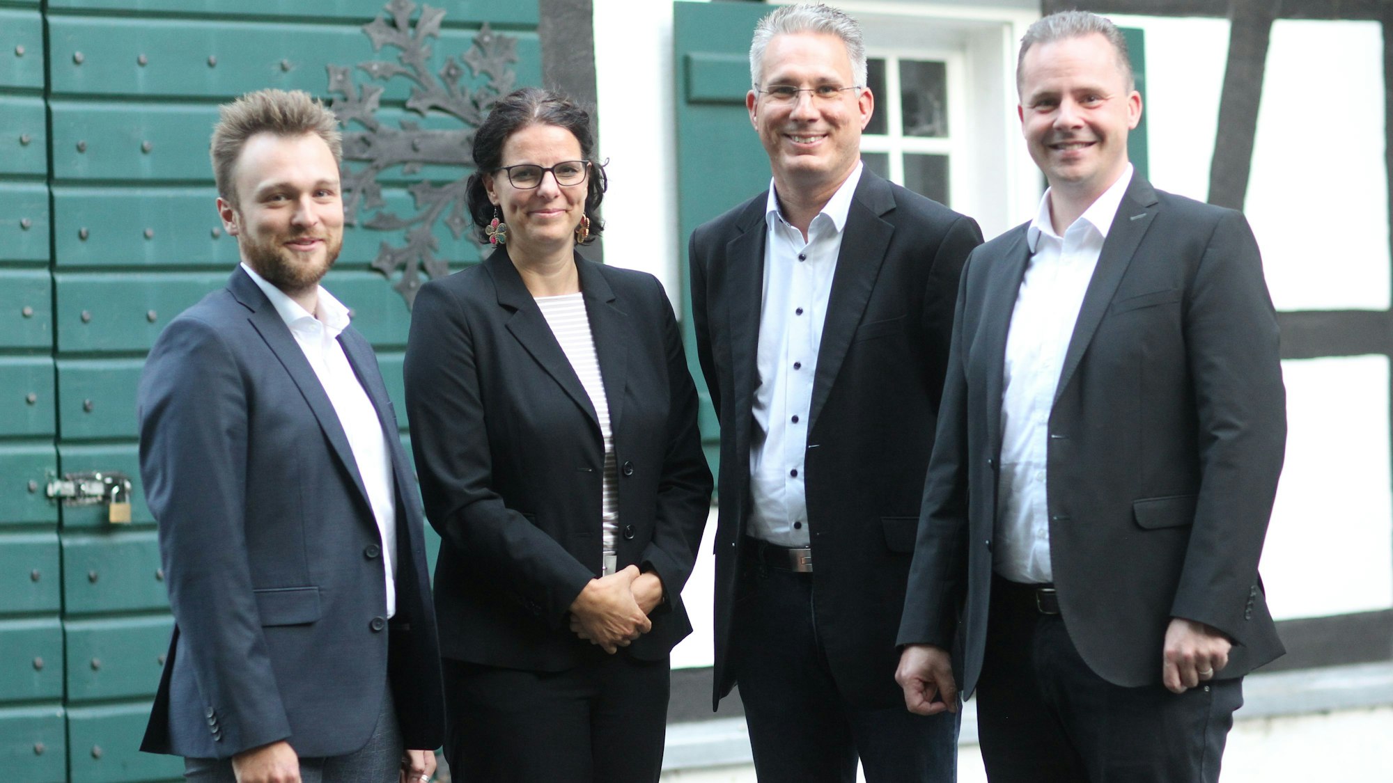 Eine Frau in einem dunklen Kostüm und drei Männer in grauen Anzügen