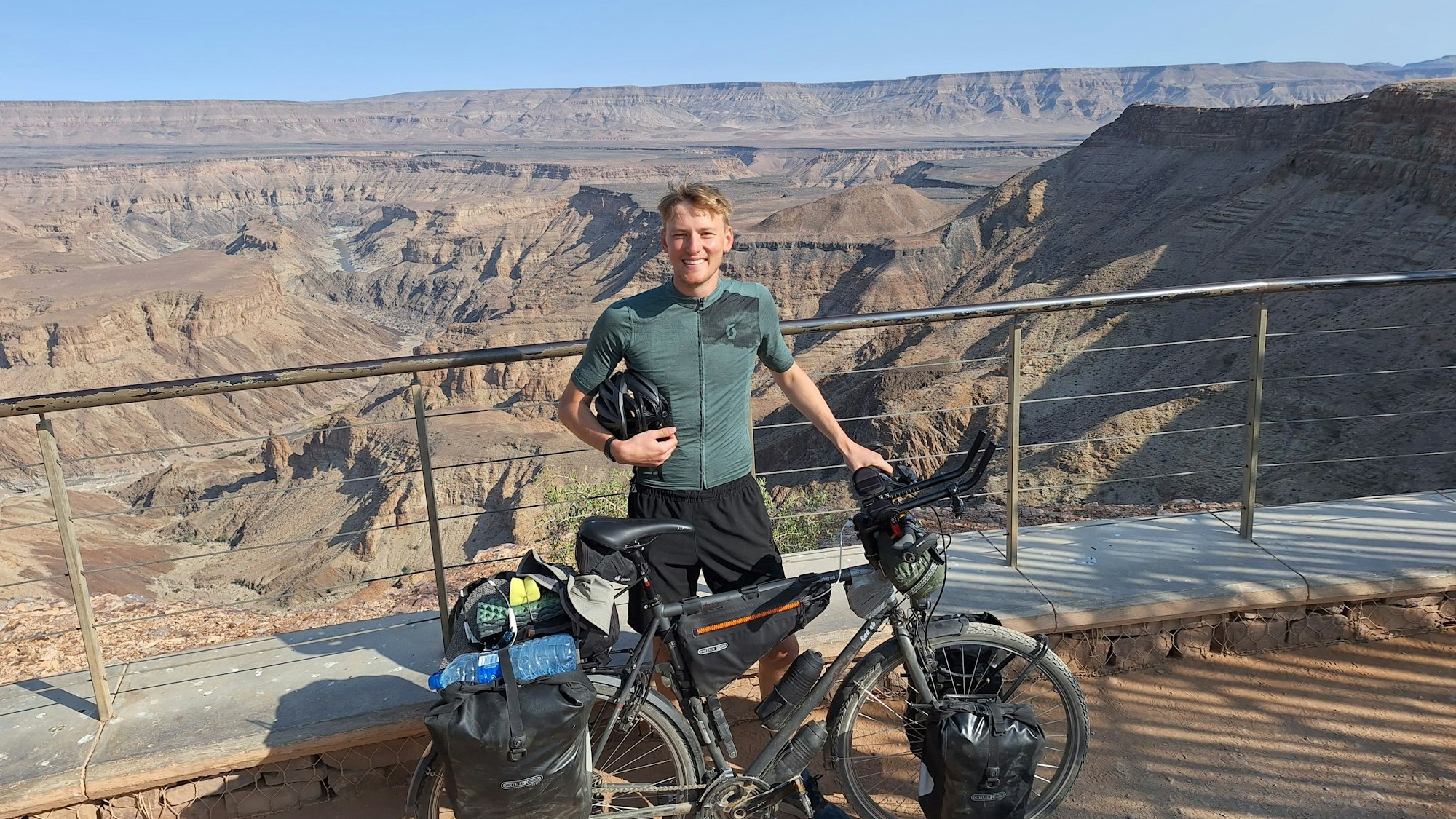 Ein junger Mann steht mit Fahrrad vor einem Canyon