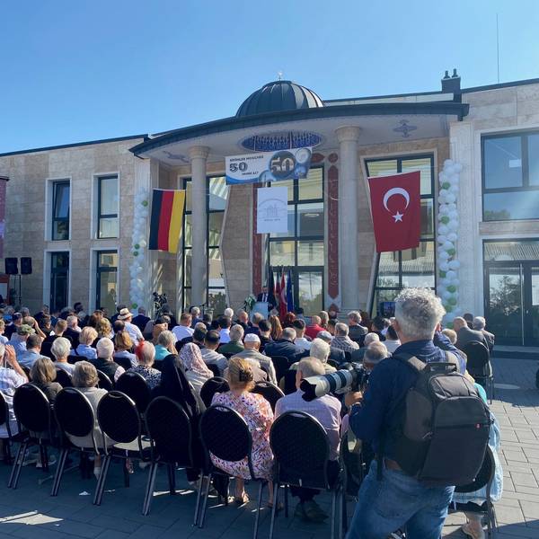 Zu sehen sind vollbesetzte Stuhlreihen vor der neuen Moschee.