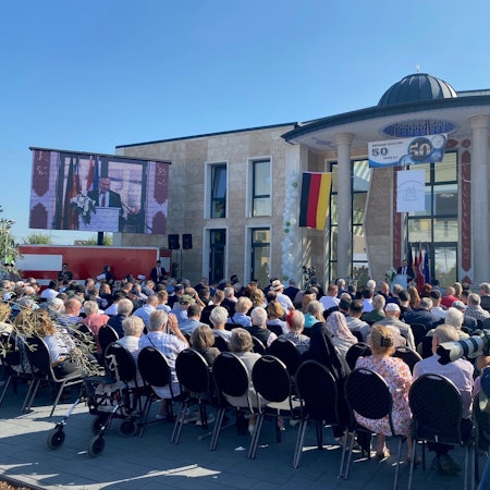Zu sehen sind vollbesetzte Stuhlreihen vor der neuen Moschee.
