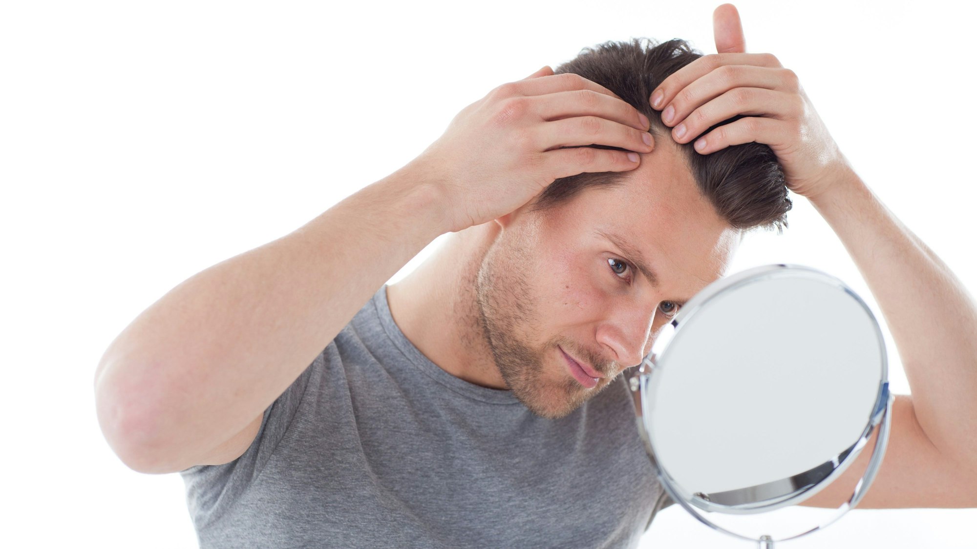 Ein Mann steht vor einem kleinen Spiegel und betrachtet seinen Haaransatz.