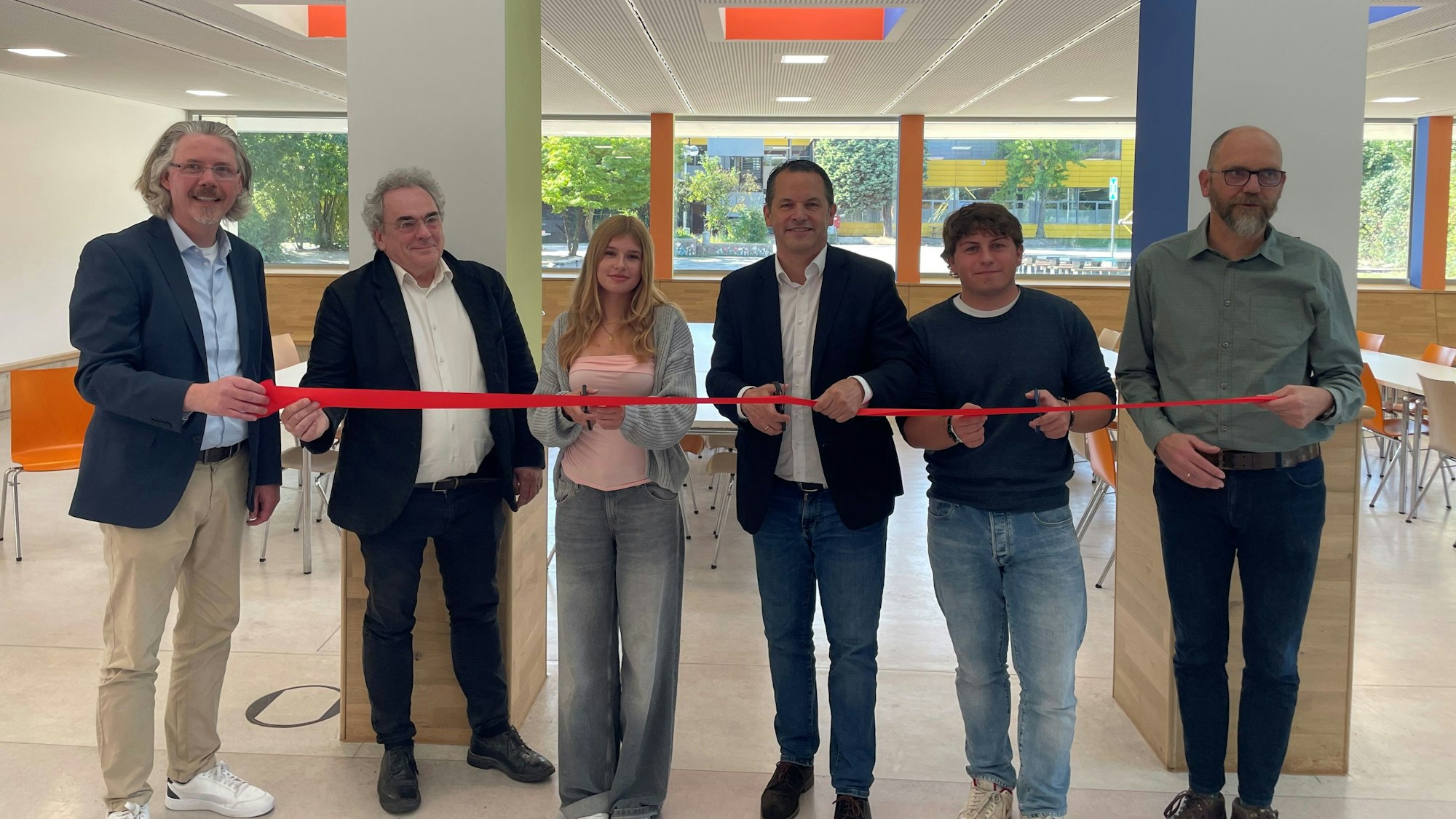 Auf dem Bild ist zu sehen, wie das rote Band zur Einweihung der neuen Mensa durchgeschnitten wird.