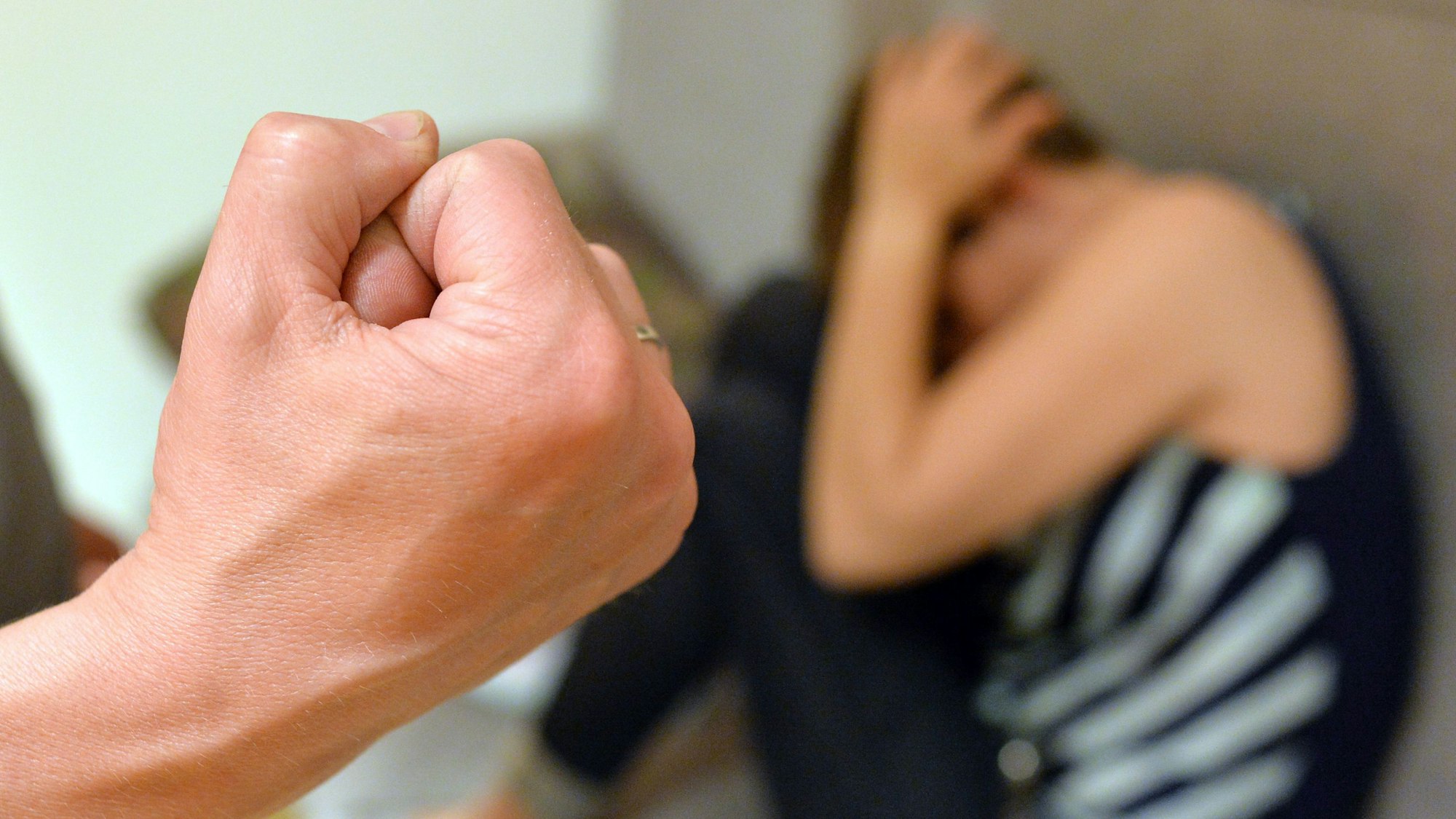 Zu sehen ist eine Frau, die sich vor der erhobenen Faust eines Mannes zu schützen versucht. Es handelt sich um eine gestellte Szene.