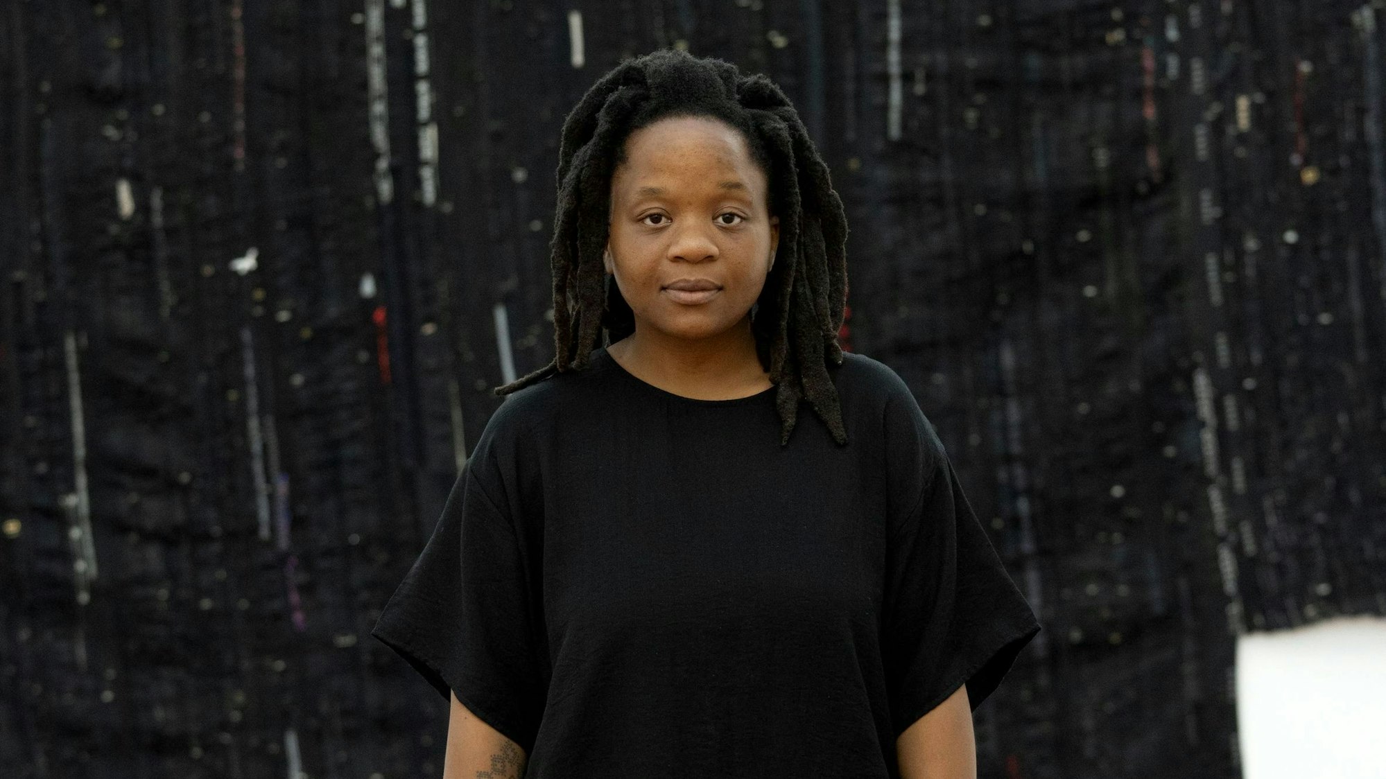 Kresiah Mukwazhi posiert in Schwarz vor einem schwarzen Kunstwerk