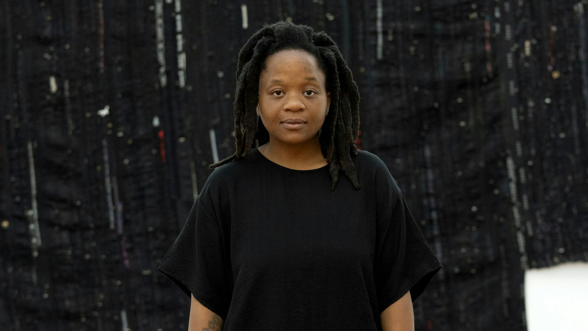 Kresiah Mukwazhi posiert in Schwarz vor einem schwarzen Kunstwerk