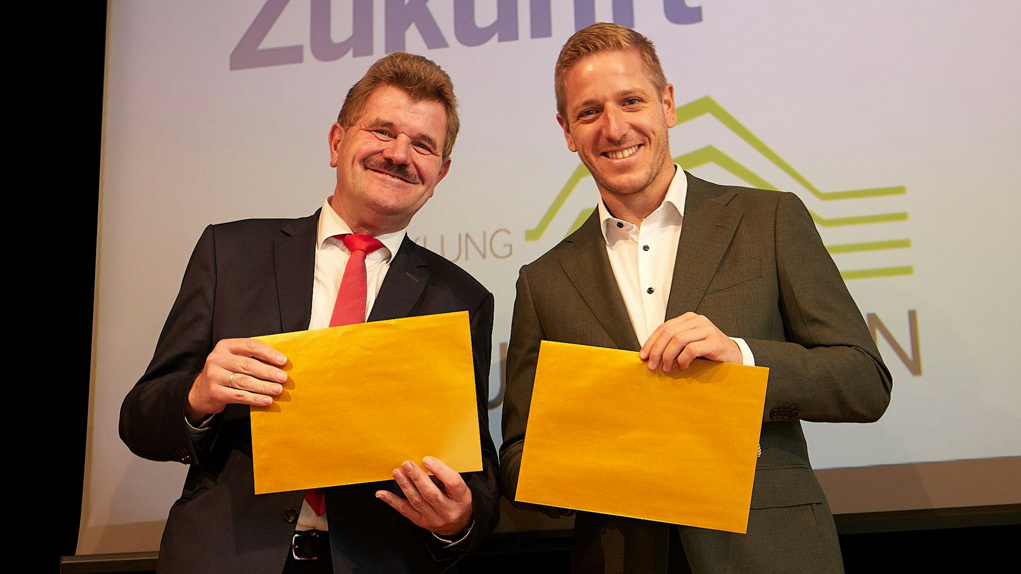 Karl-Heinz Daniels und Markus Ramers hatten die goldfarbenen Umschläge, in denen die Namen der neuen Golddörfer waren, in den Händen.
