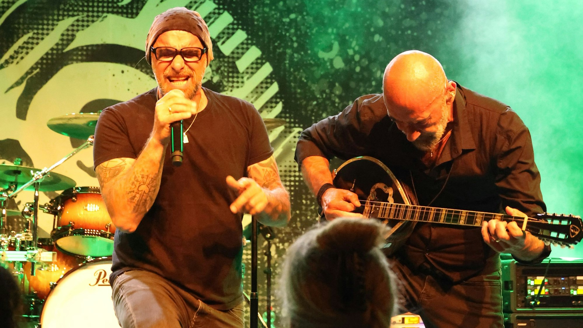 Zwei Männer singen und spielen Bouzouki auf einer Bühne.