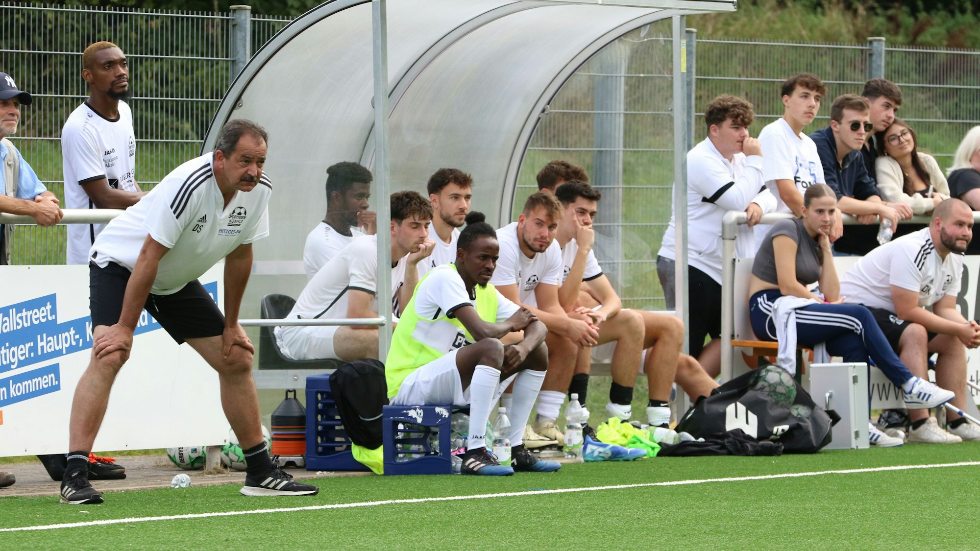 Trainer Dirk Scheer steht, nach vorne gebeugt und die Hände auf die Knie gelegt, neben der Ersatzbank.