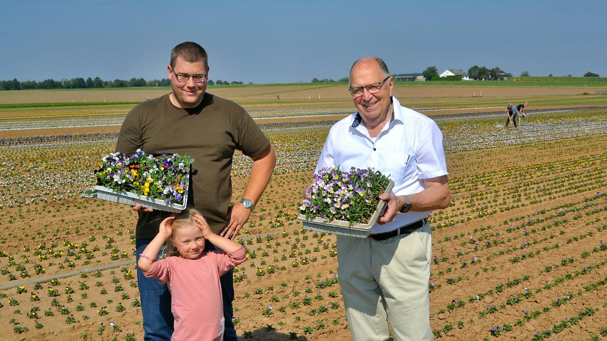 Landwirt Markus Kurth, Tochter Romy und der stellvertretende Landrat Leo Wolter präsentierten auf einem Feld die erste Stiefmütterchenernte.