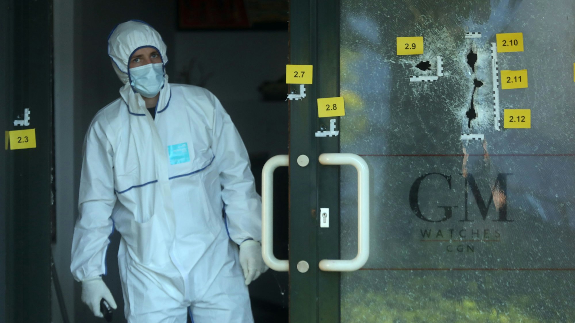 Einschusslöcher an einer Scheibe eines Uhrengeschäfts. Sie sind versehen mit gelben Markierungszetteln der Polizei.