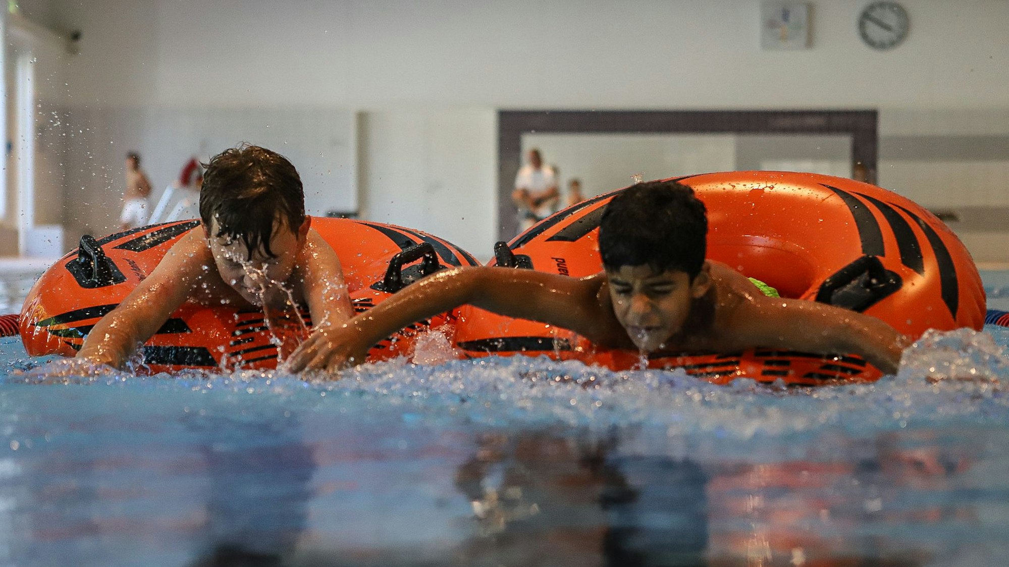Zwei Jungen versuchen in großen Schwimmreifen möglichst schnell vorwärts zu kommen.