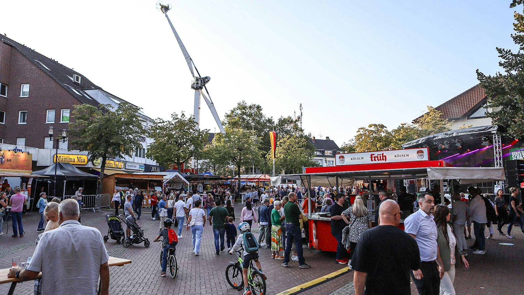 Menschen gehen über einen Platz mit Ständen, im Hintergrund ein Fahrgeschäft.