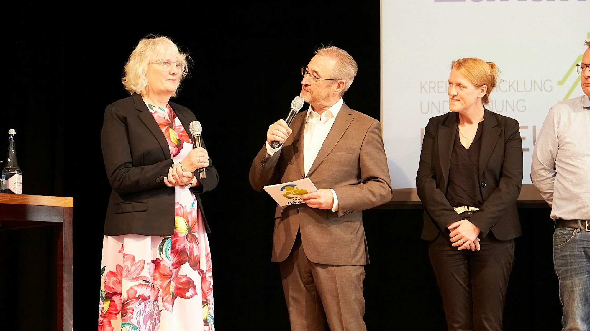 Heike Schmitz (links) und Norbert Jeub stehen mit Mikrofonen auf der Bühne.