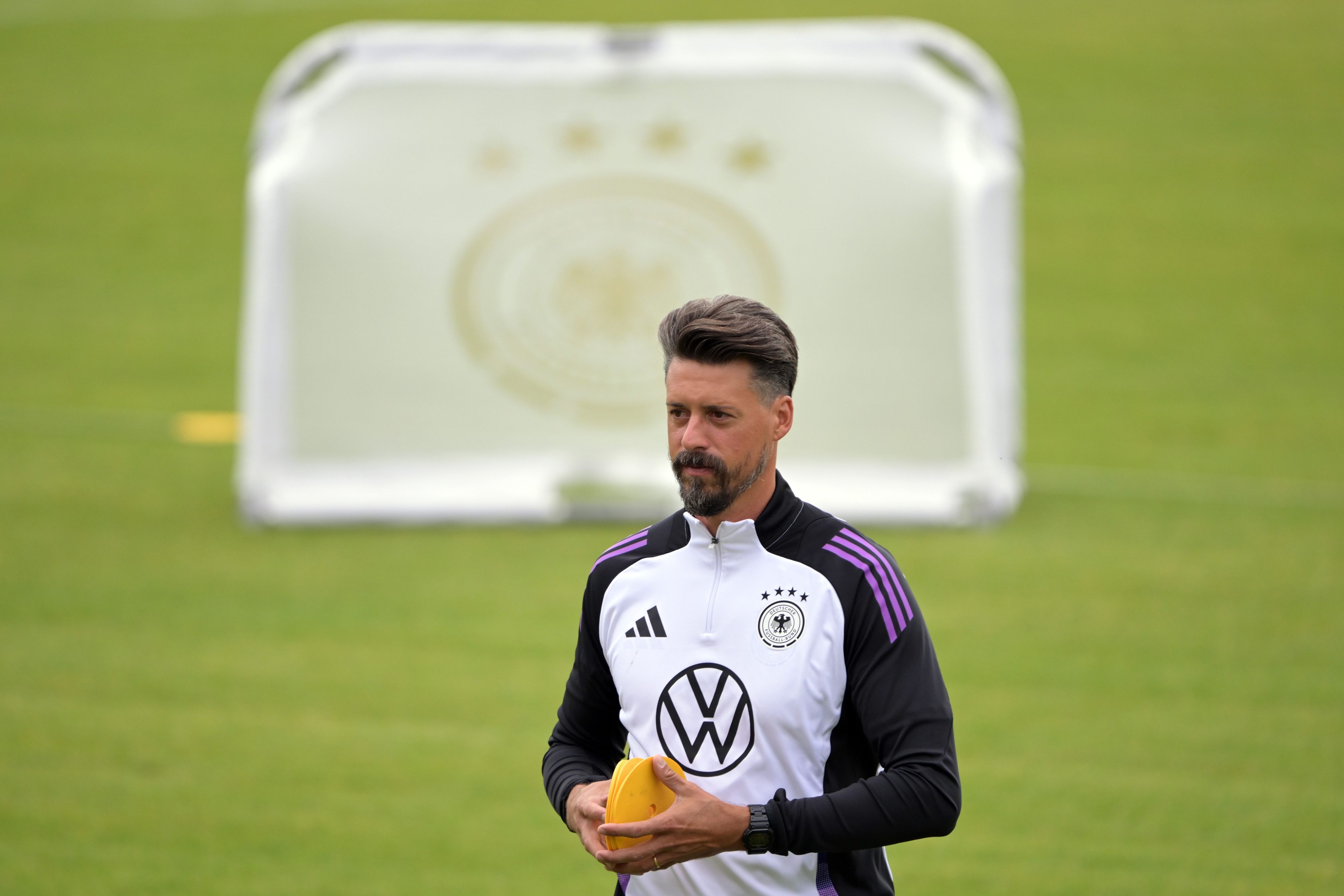Deutschlands Co-Trainer Sandro Wagner während eines öffentlichen Trainings auf dem Fußballplatz. Er trägt Trainingskleidung, im Hintergrund ist ein Tor zu sehen.