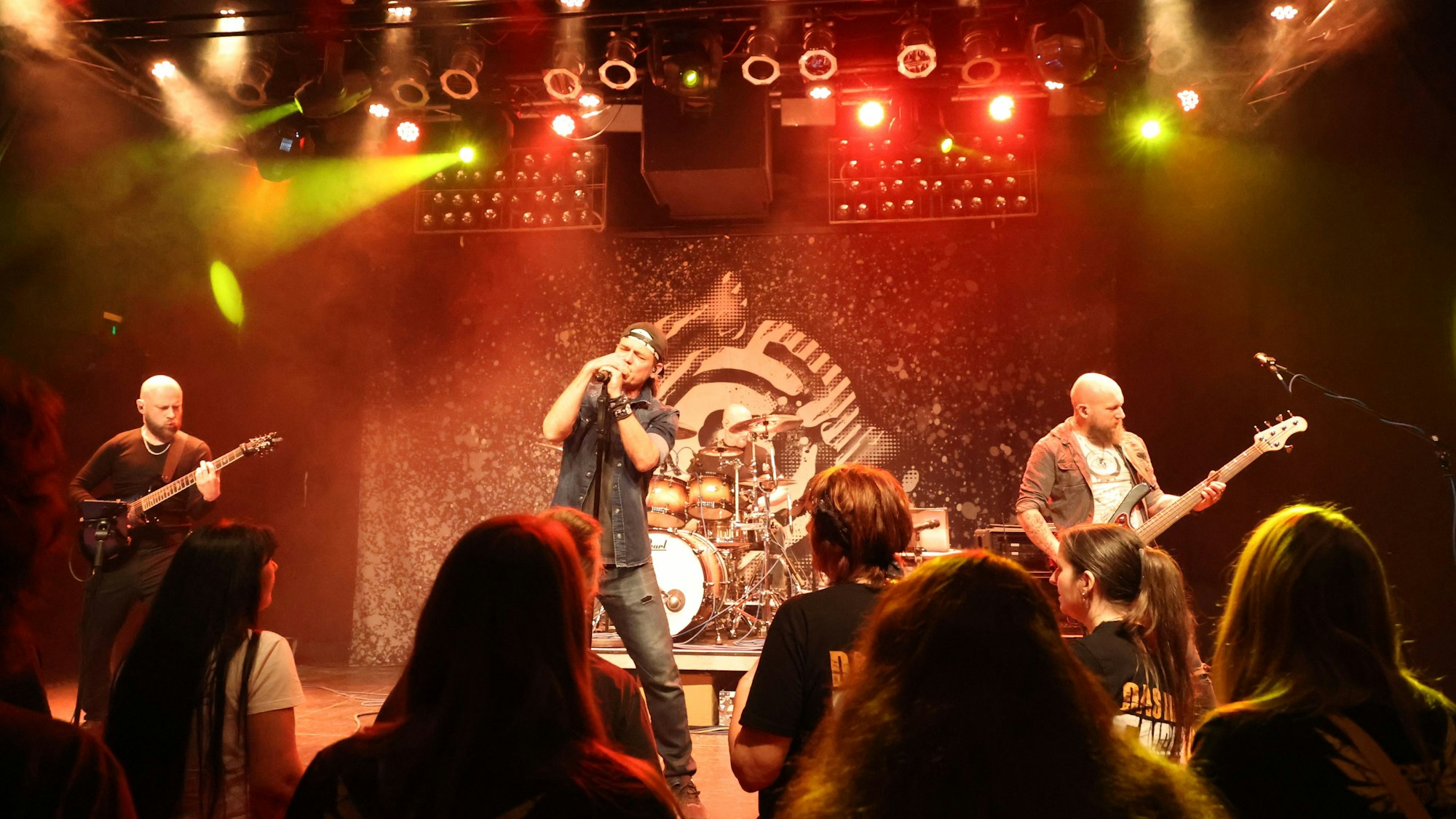 Eine Rockband spielt auf einer Bühne, vor der Leute stehen.