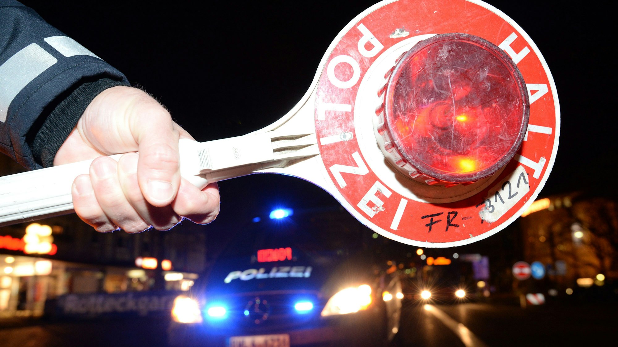 Eine Haltekelle der Polizei ist bei einer Alkoholkontrolle vor einem Polizeifahrzeug zu sehen.