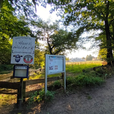 Eine umzäunte Wiese an einem Waldweg mit einem Hinweisschild