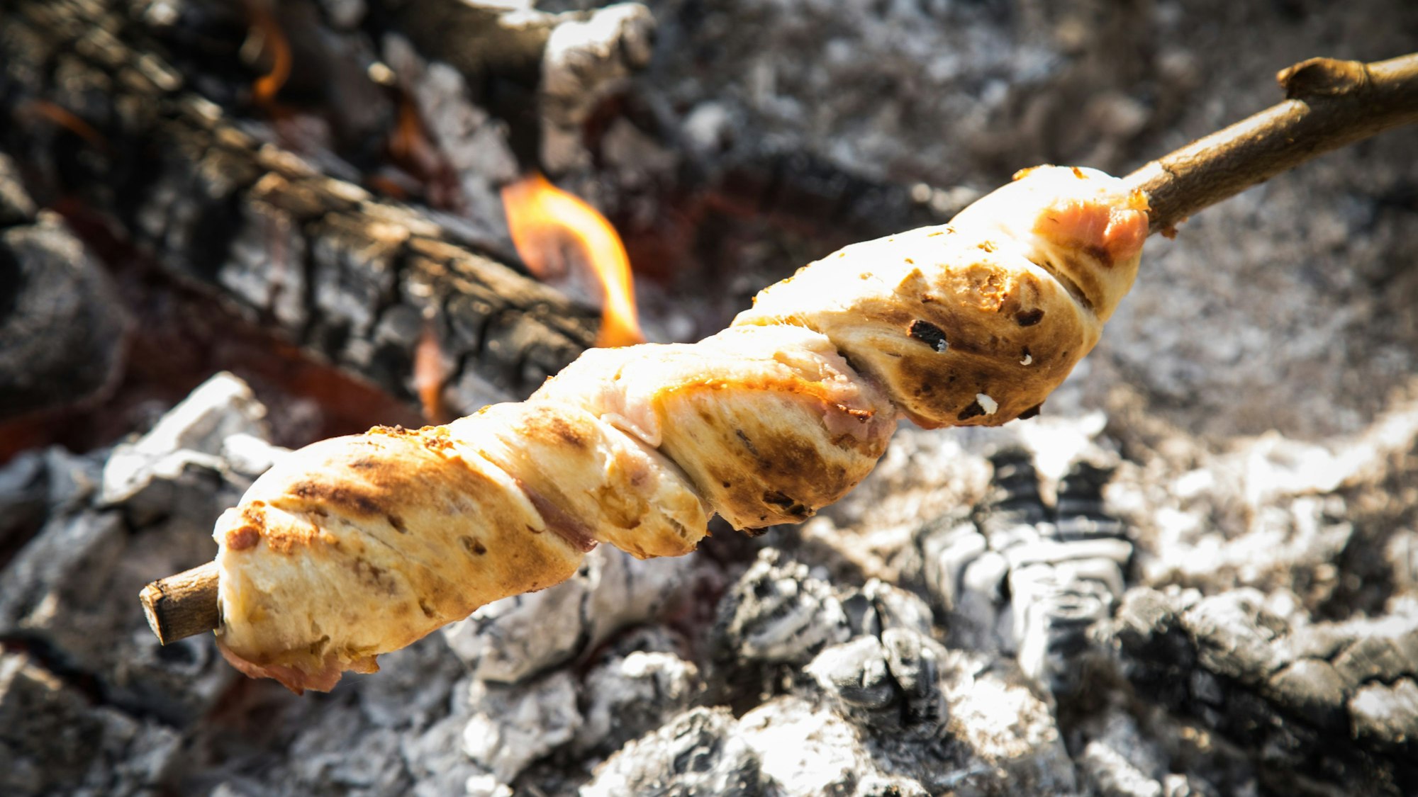 Stockbrot mit Zwiebeln und Bacon über der Glut.