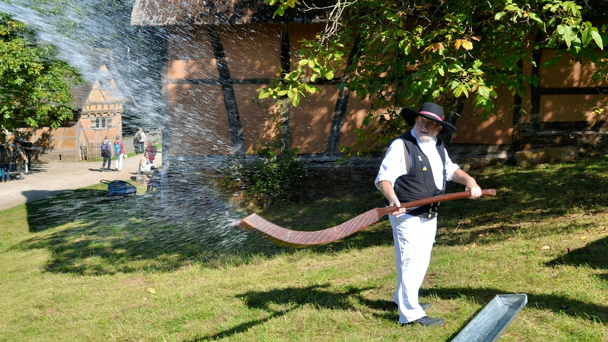 Ein Mann mit Hut schleudert Wasser mit einem historischen Werkzeug.