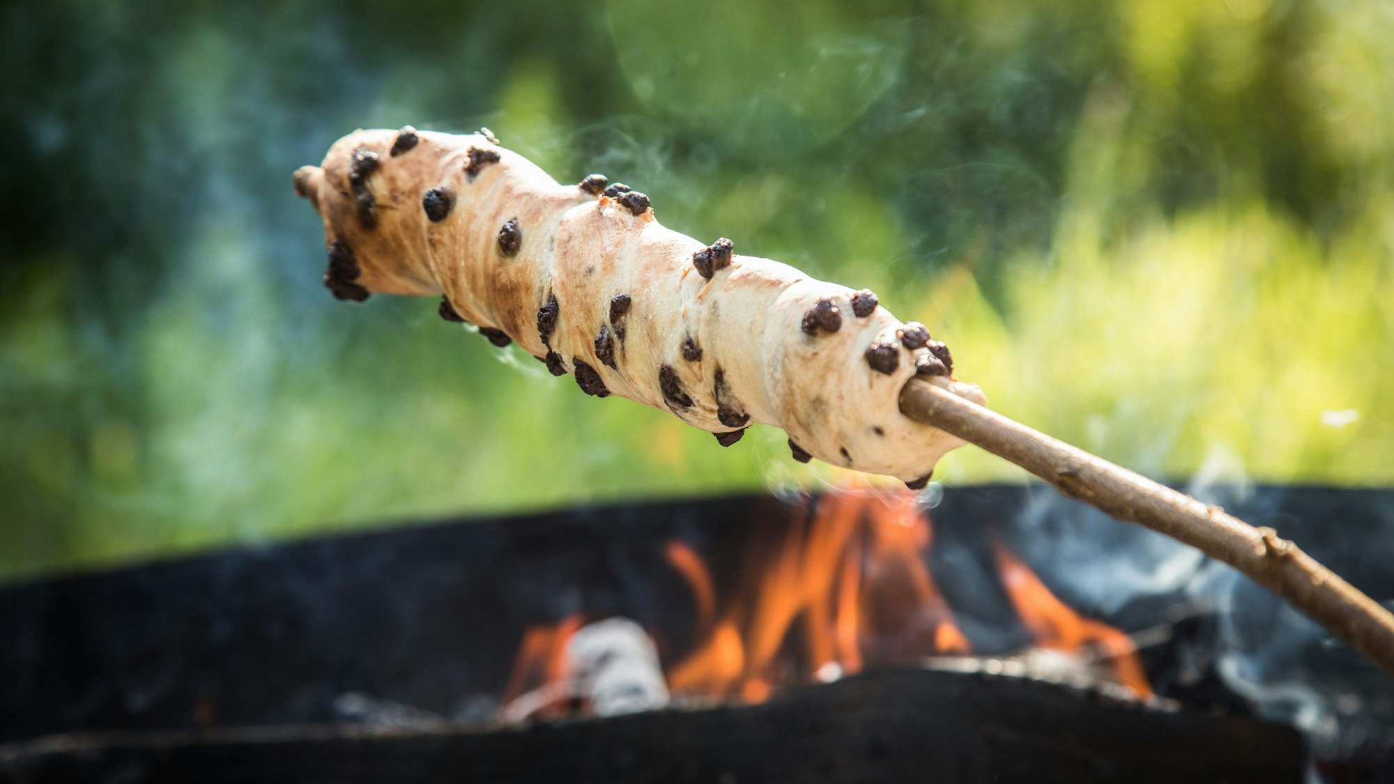 Ein Stockbrot-Teig mit Schokoladendrop wird über dem Feuer gebacken.