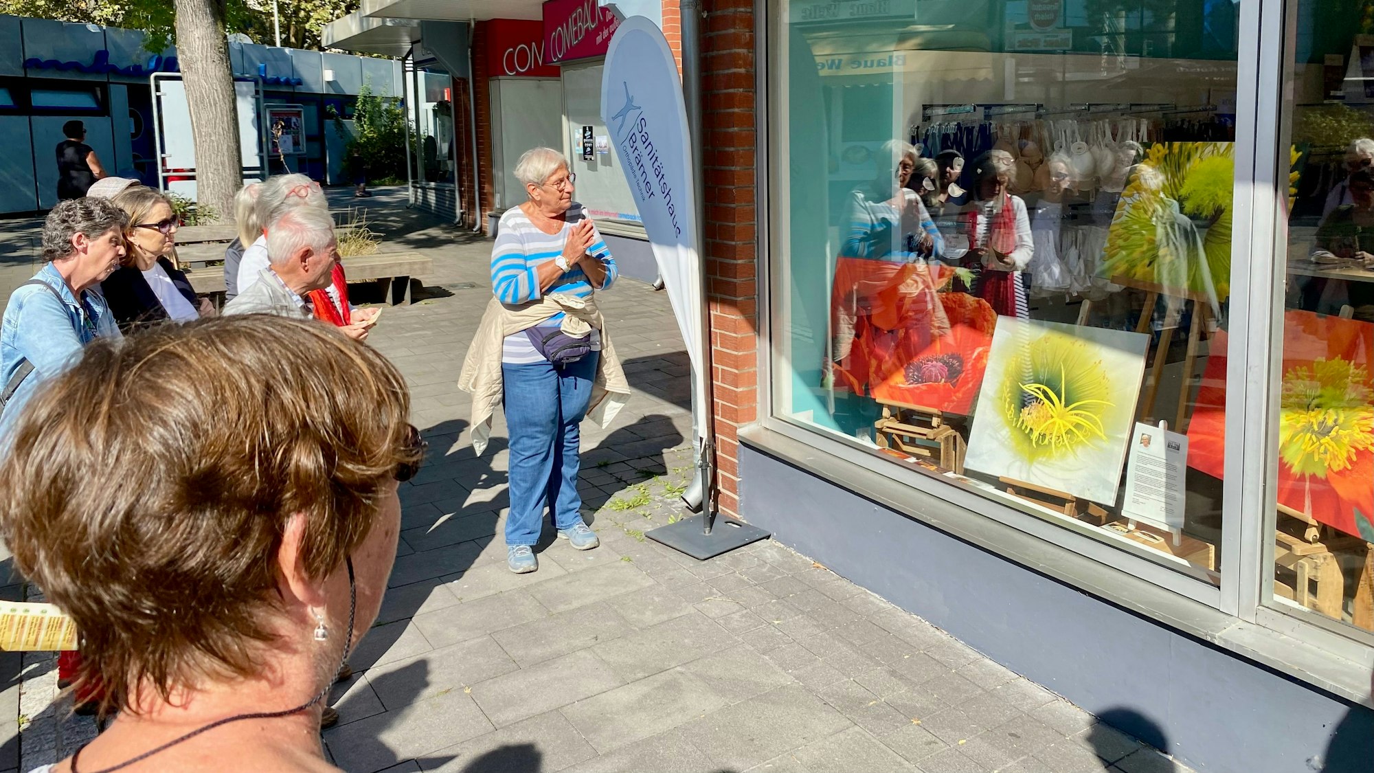 Einige Personen stehen um ein Schaufenster herum, das Gemälde in Herbstfarben zeigt.