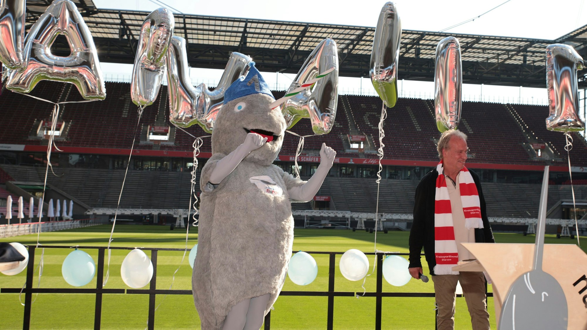 Das Bild zeigt einen Mann und ein Narwal-Maskottchen im Stadion.