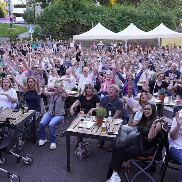 Das Foto zeigt vollbesetzte Reihen des Publikums bei einer Veranstaltung im Kulturbiergarten unter freiem Himmel.