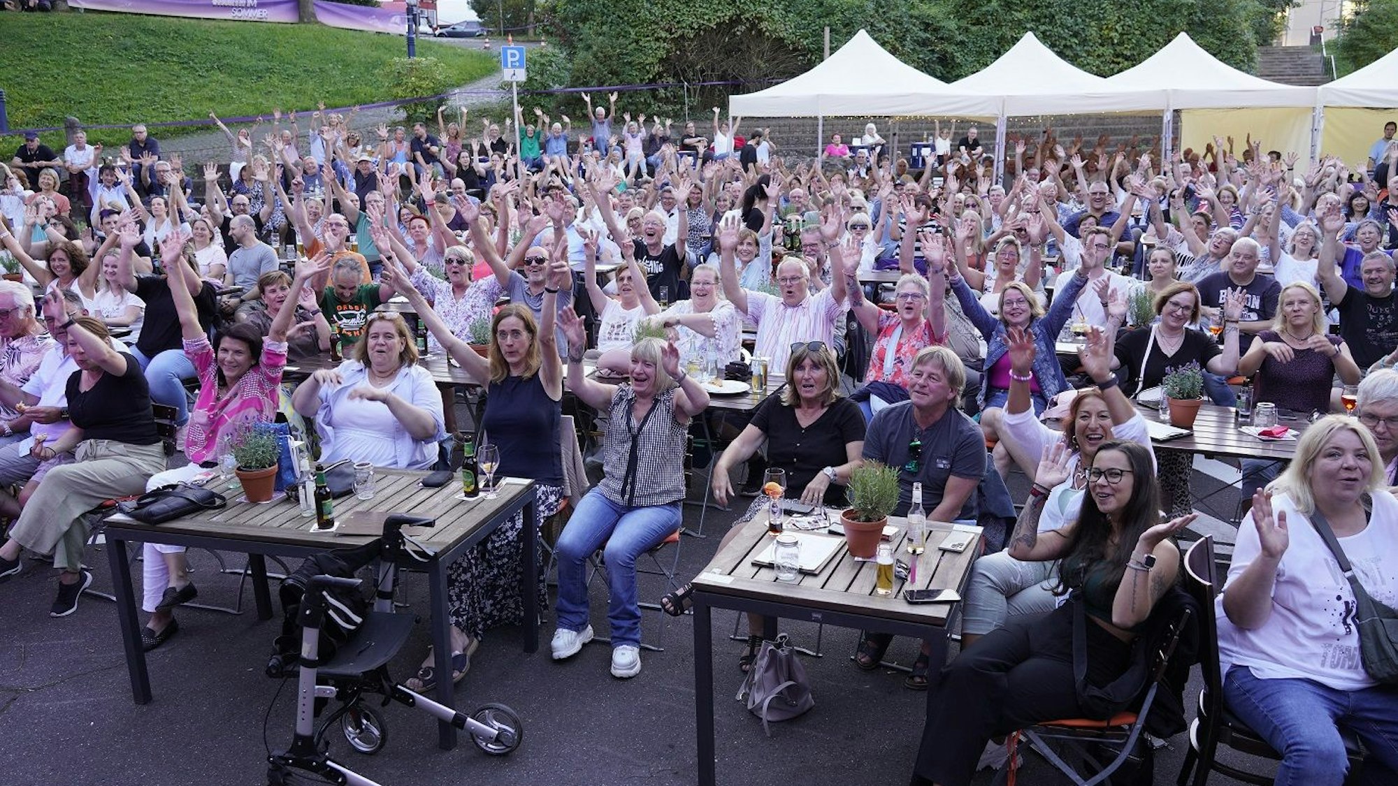 Das Foto zeigt vollbesetzte Reihen des Publikums bei einer Veranstaltung im Kulturbiergarten unter freiem Himmel.